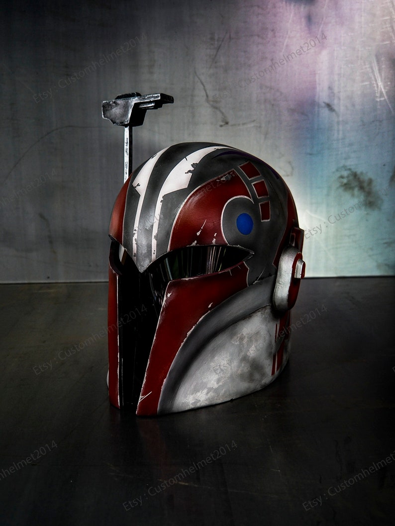 May include: A red, gray, and white helmet with a blue and white design on the side. The helmet has a black visor and a metal antenna on top.