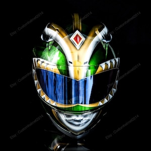 May include: A green and gold motorcycle helmet with a painted design of a Power Ranger. The helmet has a blue visor and a white stripe across the top.