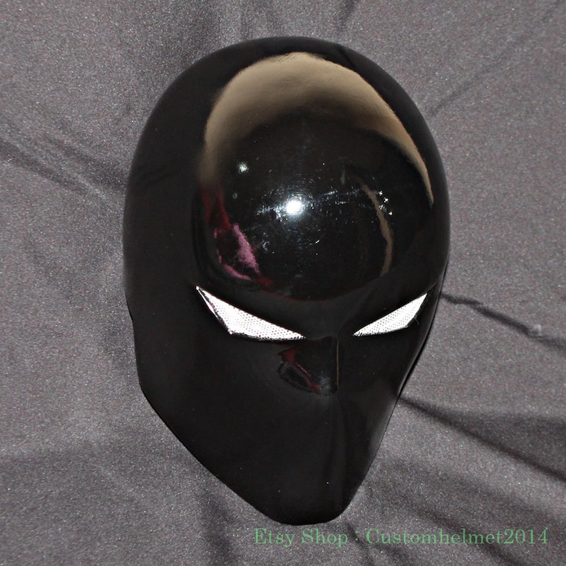 Pu&ograve; includere: Un casco nero lucido con dettagli bianchi per gli occhi. Il casco ha una superficie liscia e riflettente e un design aerodinamico. Il nome del negozio Etsy "Customhelmet2014" &egrave; visibile in basso.