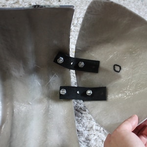 May include: Two pieces of a gray fiberglass motorcycle fairing with black metal brackets and screws. The fairing pieces are joined together.