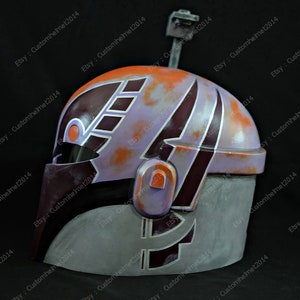 May include: A close-up of a purple, orange, and gray helmet with a black visor. The helmet has a design of stripes and geometric shapes.