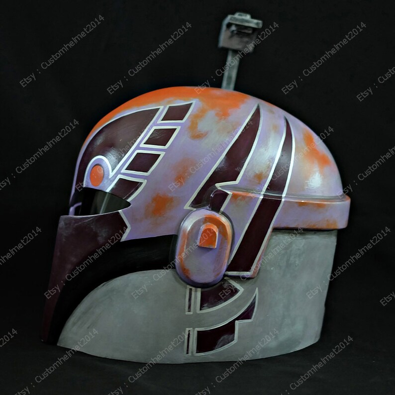 May include: A close-up of a purple, orange, and gray helmet with a black visor. The helmet has a design of stripes and geometric shapes.