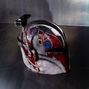 May include: A white, red, and blue helmet with a weathered finish. The helmet has a black visor and a black antenna on top. The helmet is sitting on a gray surface.
