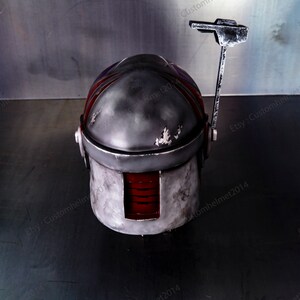 May include: A gray and red helmet with a weathered finish and a small antenna on top. The helmet has a red visor and a black stripe on the side. The helmet is sitting on a gray surface. Etsy: Customhelmet2014