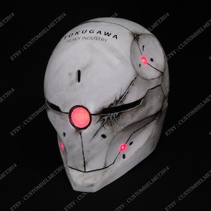 May include: A white helmet with a weathered, distressed look. The helmet has a black visor and red LED lights. The text "TOKUGAWA HEAVY INDUSTRY" is printed on the top of the helmet.
