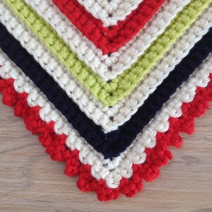 May include: Close-up of a crocheted corner with a scalloped edge. The crochet is made in white, red, green, and navy blue yarn.