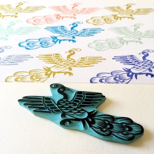 May include: A blue rubber stamp of a stylized peacock with black details. The stamp is on a white surface with several printed images of peacocks in various colors.