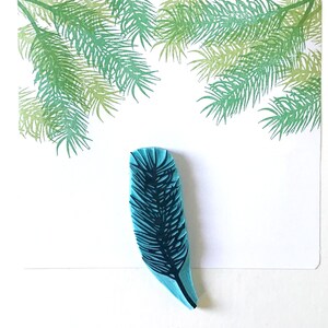 May include: A blue rubber stamp with a detailed design of a pine branch. The stamp is on a white background.