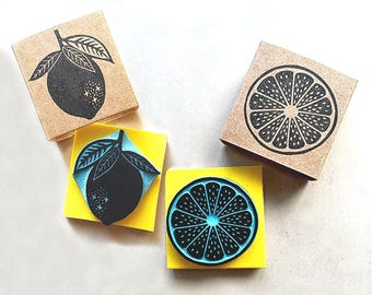 May include: Four rubber stamps with fruit designs. Two stamps feature a whole lemon with leaves, and two show a lemon slice. The stamps are black and blue on yellow pads, and brown on the stamp blocks.