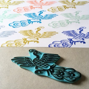 May include: A teal blue wooden block carving of a peacock with black detailing. The peacock is facing right with its wings spread and its tail feathers fanned out.