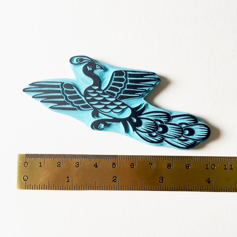 May include: A blue rubber stamp with a black silhouette of a stylized bird with a long tail. The stamp is approximately 7 inches long.