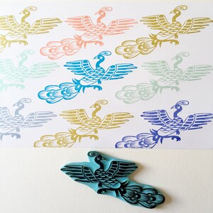 May include: A set of 10 rubber stamps featuring a stylized peacock design in various colors, including blue, green, gold, pink, and purple. The stamps are arranged in a grid pattern on a white background.