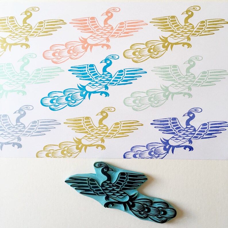 May include: A set of 10 rubber stamps featuring a stylized peacock design in various colors, including blue, green, gold, pink, and purple. The stamps are arranged in a grid pattern on a white background.