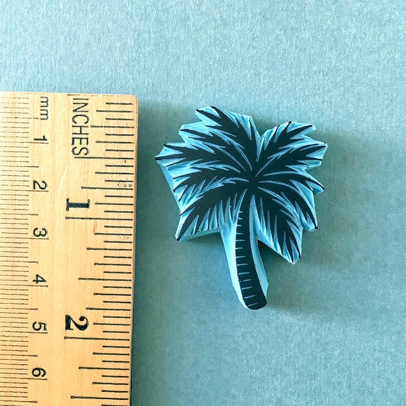 May include: A blue rubber stamp of a palm tree with a black silhouette. The stamp is approximately 1 inch tall.