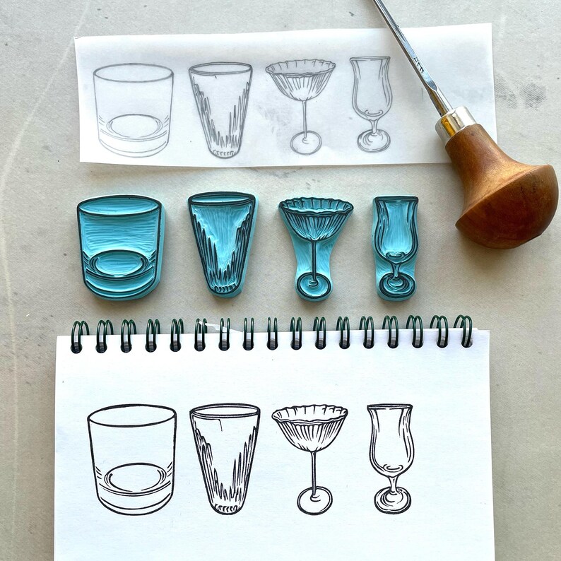 May include: Four blue rubber stamps showing designs of various glasses: a tumbler, a highball, a cocktail glass, and a hurricane glass. A carving tool with a wooden handle and sketches of the glassware are also visible.