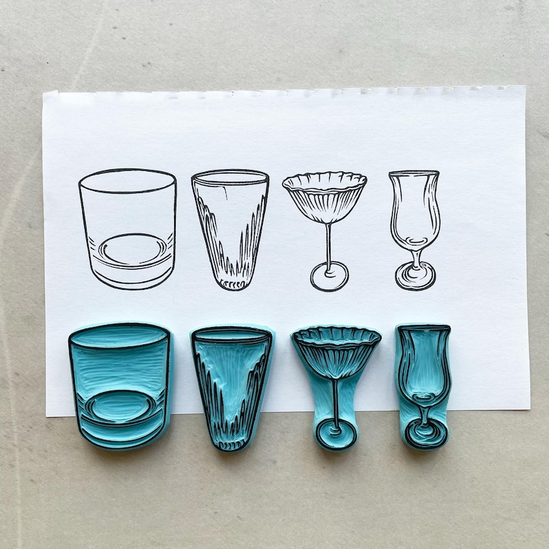 May include: Four different drink glass designs are illustrated in black ink on white paper. Below, the same four glass designs are shown as blue rubber stamps. The glasses include a rocks glass, a tall glass, a stemmed cocktail glass, and a tulip glass.