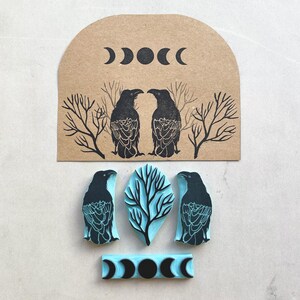 Puede incluir: Un conjunto de sellos de goma con tem&aacute;tica celestial y natural. Los sellos incluyen dos cuervos negros, un &aacute;rbol y fases lunares. Los sellos son de color negro y azul claro.