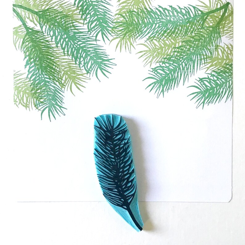 May include: A blue rubber stamp with a detailed design of a pine branch. The stamp is on a white background.