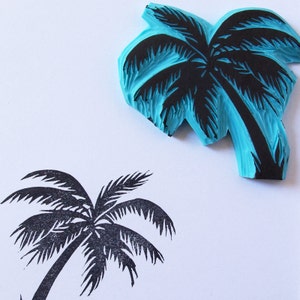 May include: A blue rubber stamp with a black palm tree design. The stamp is used to create a palm tree image on paper.