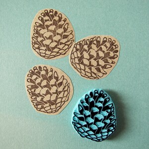 May include: Four pine cone stamps, three are brown and one is blue. The brown stamps are on a light blue background. The blue stamp is on a white background.