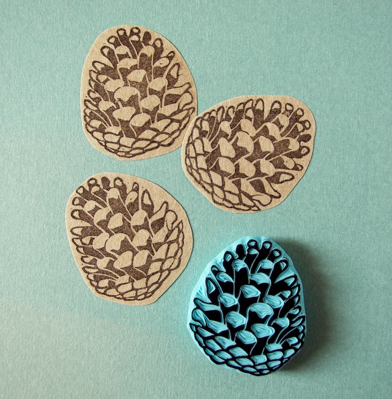 May include: Four pine cone stamps, three are brown and one is blue. The brown stamps are on a light blue background. The blue stamp is on a white background.