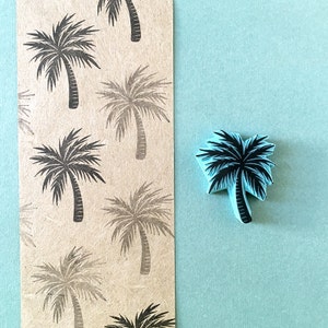 May include: A sheet of brown paper with a repeating pattern of black palm trees. A blue rubber stamp of a palm tree is on a light blue background.