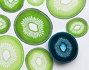 May include: A set of ten green and white rubber stamps featuring a kiwi fruit design. The stamps are arranged in a circle around a blue rubber stamp with a kiwi fruit design.