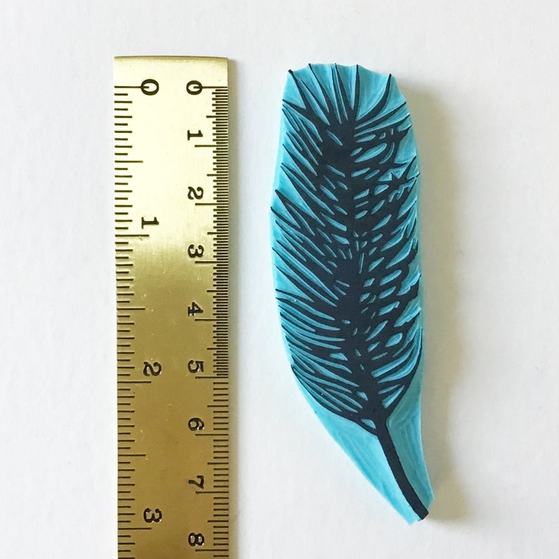 May include: A blue rubber stamp with a black silhouette of a feather. The stamp is approximately 2 inches tall.