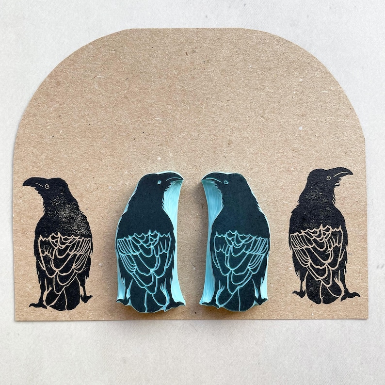 Puede incluir: Cuatro grabados de arte de cuervos negros sobre un fondo marr&oacute;n claro. Dos cuervos se enfrentan con detalles en azul claro, mientras que los otros dos son negros s&oacute;lidos. Los grabados tienen patrones de plumas detallados y est&aacute;n sobre un fondo semicircular.