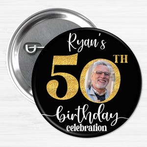 May include: A black and gold button with a photo of a man and the text "Ryan's 50th birthday celebration".