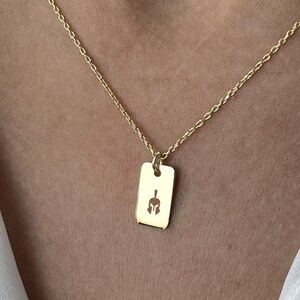 Könnte beinhalten: Eine goldene Kettenkette mit einem kleinen rechteckigen Anhänger, der ein ausgeschnittenes Design eines spartanischen Helms zeigt.