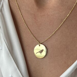 Könnte beinhalten: Eine goldene Kettenkette mit einem runden Anhänger, der eine Silhouette eines Vogels zeigt.