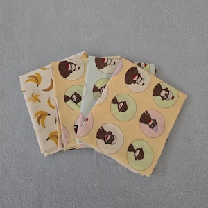 May include: Four fabric squares with different patterns. One features bananas, while the others have a repeating design of a sock monkey in a circle. The background colors vary from cream to light yellow and blue.
