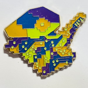May include: A gold-colored enamel pin with a circuit board design. The pin is made up of yellow, blue, purple, and green squares and circles.