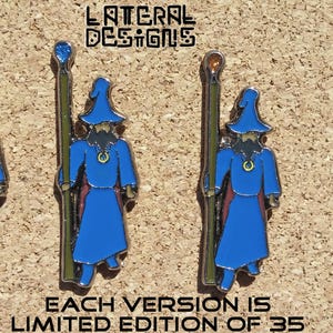 Peut inclure: Quatre épingles émaillées représentant un magicien en robe et chapeau bleus, tenant un bâton. Chaque épingle a une gemme de couleur différente sur le dessus du bâton. Le texte "LATERAL DESIGNS" et "EACH VERSION IS LIMITED EDITION OF 35" sont également visibles.