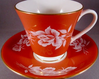 May include: A red teacup and saucer set with white floral designs. The cup and saucer have a gold trim.