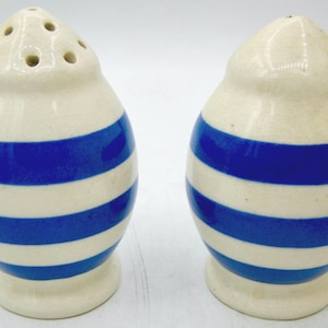 May include: A pair of egg-shaped ceramic salt and pepper shakers featuring a glossy off-white base color with horizontal royal blue stripes. One shaker has multiple small holes at the top, while the other has a single small hole at the top.