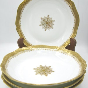 May include: A collection of white porcelain bowls featuring gold rims and a gold floral centre design. The bowls have a scalloped edge and are stacked. The gold trim has a detailed pattern, adding to the elegance of the tableware.