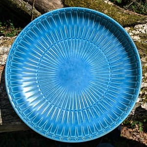 May include: A large, round, blue ceramic serving dish with a sunburst pattern. The dish has a deep blue glaze and a raised, textured design.