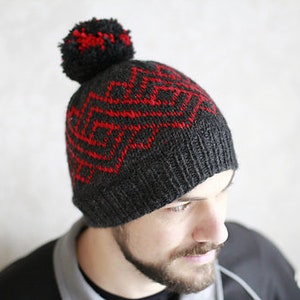 May include: A gray knitted beanie with a red geometric pattern and a black pom pom on top.