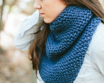 May include: A woman wearing a blue knitted scarf. The scarf is a simple design with a textured knit.