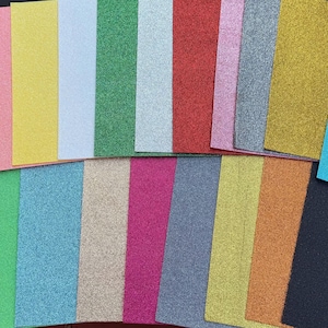 May include: A collection of colorful glitter cardstock sheets in various shades, including purple, pink, yellow, blue, green, silver, red, and gold. The sheets are arranged in a neat, organized display, perfect for crafting projects.