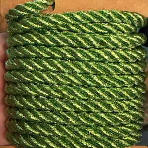 May include: A spool of metallic lime green twisted cord wrapped around a rectangular cardboard base. The cord features a shiny, reflective finish with a distinct braided texture, wound in multiple horizontal rows across the flat support.