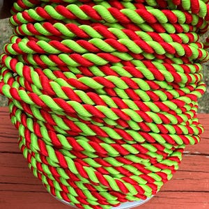 May include: Close-up of a tightly coiled rope. The rope is a vibrant combination of red and lime green, twisted together in a spiral pattern. The rope is thick and appears to be made of a durable material, suitable for various crafting or decorative purposes.