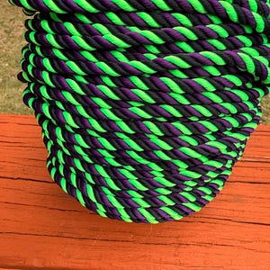 May include: Close-up of a coiled rope with alternating bands of neon green, black, and purple. The rope is tightly wound, creating a textured surface. The color combination gives the rope a vibrant and eye-catching appearance.