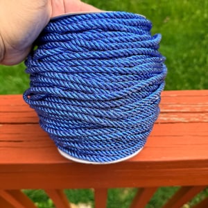May include: A spool of vibrant blue rope. The rope is tightly wound, revealing a textured surface. The color shifts slightly, creating a subtle iridescent effect. The rope is sitting on a wooden surface.