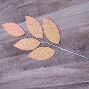 May include: A branch with five glittery peach-colored leaves, each leaf is shaped like a teardrop. The branch is made of thin wire and is perfect for adding a touch of fall to your home decor.