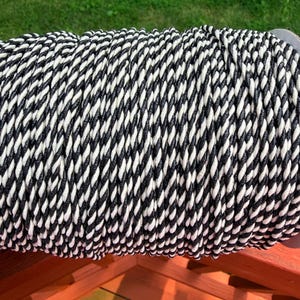 May include: A spool of thick, twisted cord featuring a repeating pattern of black and white diagonal stripes. The cord is tightly wound in multiple parallel rows, creating a textured, cylindrical shape with a consistent, uniform appearance.