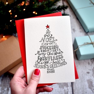 May include: A white card with a black hand-drawn Christmas tree design. The tree is made up of words related to Christmas, including "Noël", "carols", "stocking", "ribbon & gifts", "Merry Christmas", "snowflakes", "sleigh bell", and "Season's Greetings".