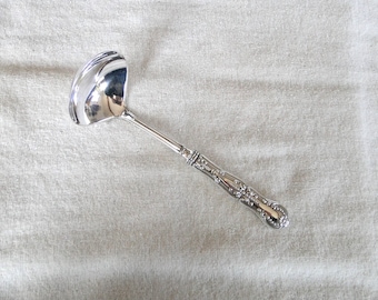 May include: A silver ladle with an ornate handle. The ladle has a rounded bowl and a long, slender handle with a decorative design.